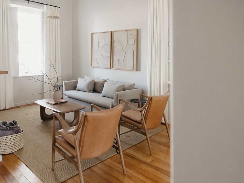 A bright and well-maintained living room featuring polished hardwood flooring and large sash windows with elegant curtain treatments.
