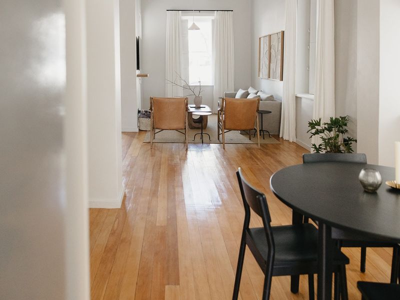 An open-plan living and dining area featuring polished hardwood flooring, neutral walls, and large windows with natural light.