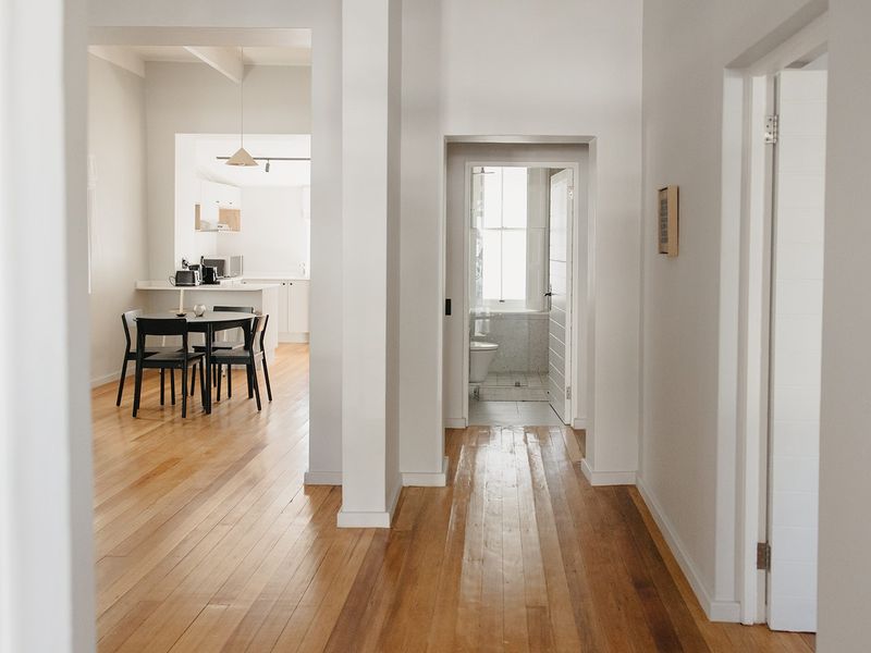 A bright hallway with polished hardwood flooring, providing access to an open-plan living area and a bathroom with modern finishes.