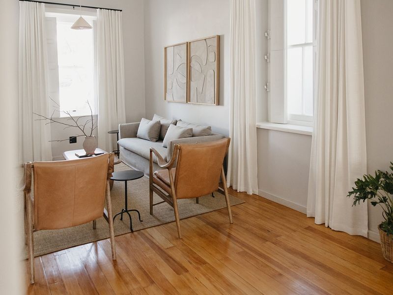 A bright and inviting living room featuring polished hardwood flooring and classic sash windows with internal shutters.