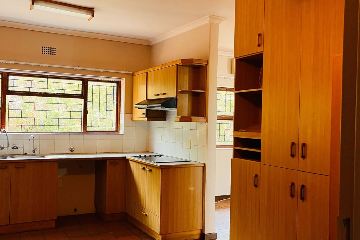 A functional kitchen featuring built-in wooden cabinetry, an electric hob, extractor fan, and tiled flooring, offering a classic layout with ample storage space.
