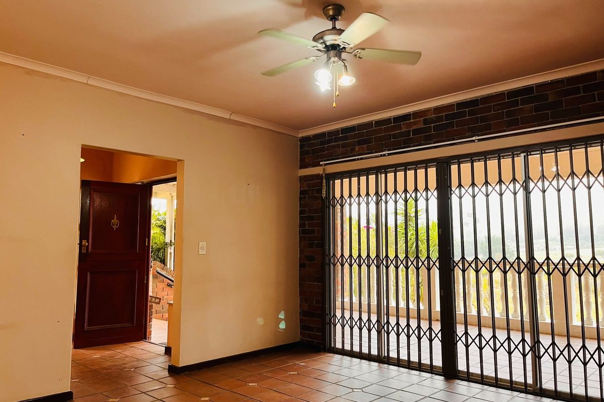Spacious living area featuring terracotta floor tiles, an exposed brick feature wall, ceiling fan, and sliding doors leading to an outdoor patio.