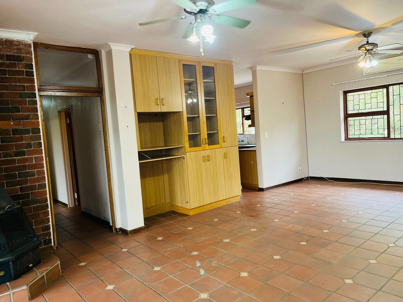 Spacious open-plan living area featuring a brick fireplace, built-in cabinetry, tiled flooring, and ceiling fans, offering a versatile layout for modern living.