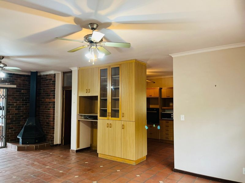 Open plan living area featuring a brick fireplace, ceiling fan, and built-in cabinetry, flowing into a functional kitchen space with tiled flooring throughout.