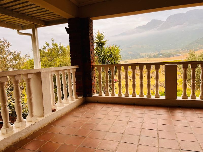 A covered balcony featuring tiled flooring and a classic balustrade railing, offering scenic mountain and landscape views.