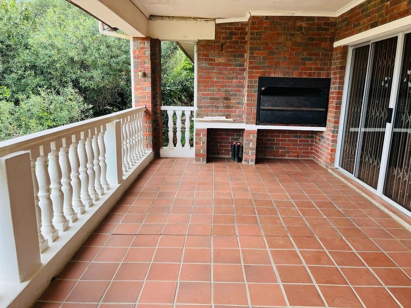 Covered patio featuring a built-in brick braai, tiled flooring, and a classic balustrade, offering a functional outdoor entertainment space.