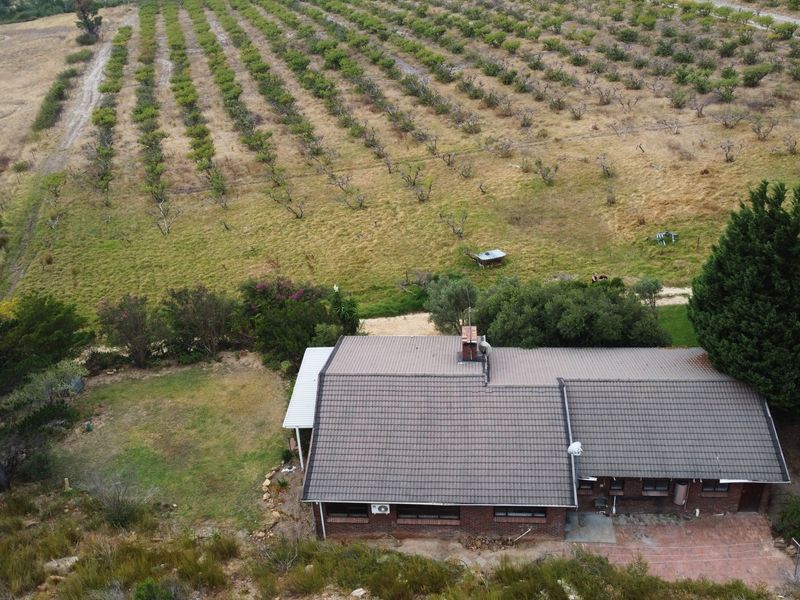 Aerial view of a brick house with a tiled roof, featuring a paved patio area and surrounding agricultural land.