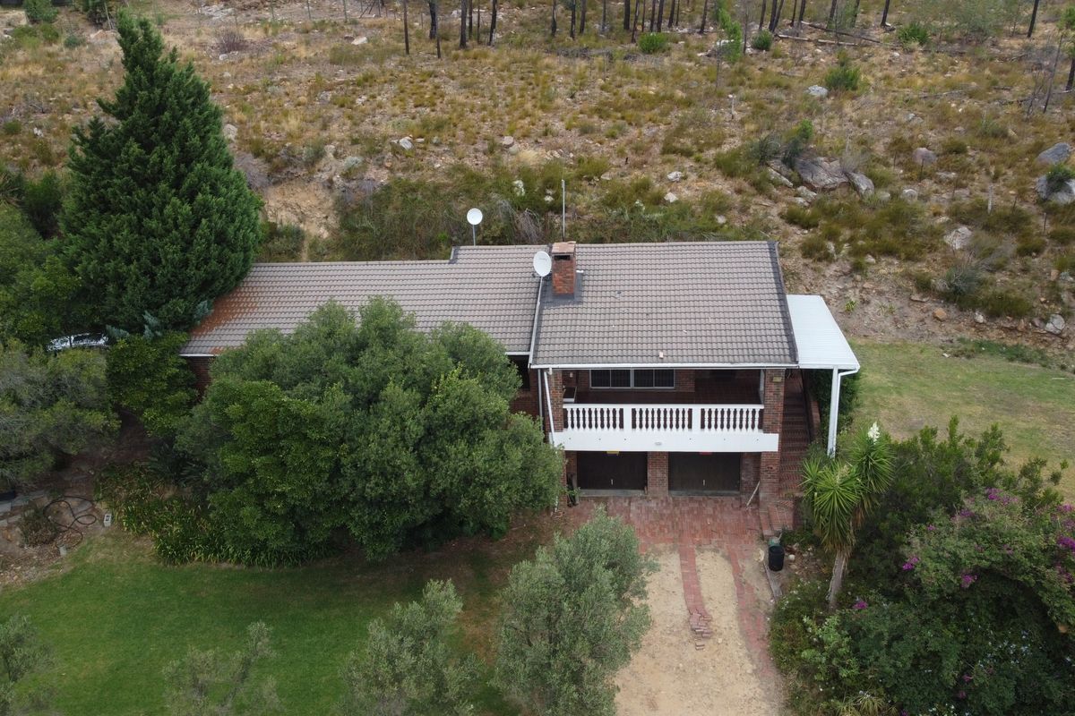 Aerial view of a brick house featuring a tiled roof, a balcony with a balustrade, and a brick driveway set against a natural landscape.