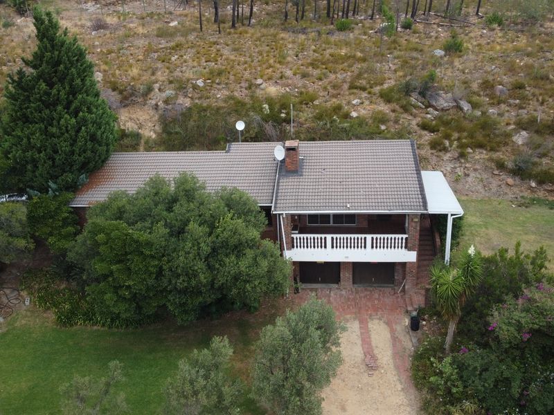 Aerial view of a brick house featuring a tiled roof, a balcony with a balustrade, and a brick driveway set against a natural landscape.