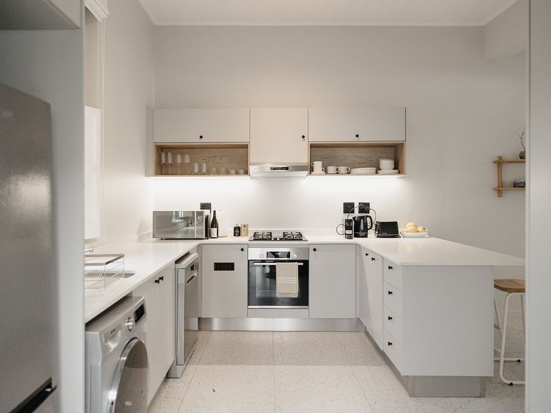 Modern, well-lit kitchen featuring sleek white cabinetry, stone countertops, integrated appliances, and stylish terrazzo flooring, offering a clean and functional culinary space.
