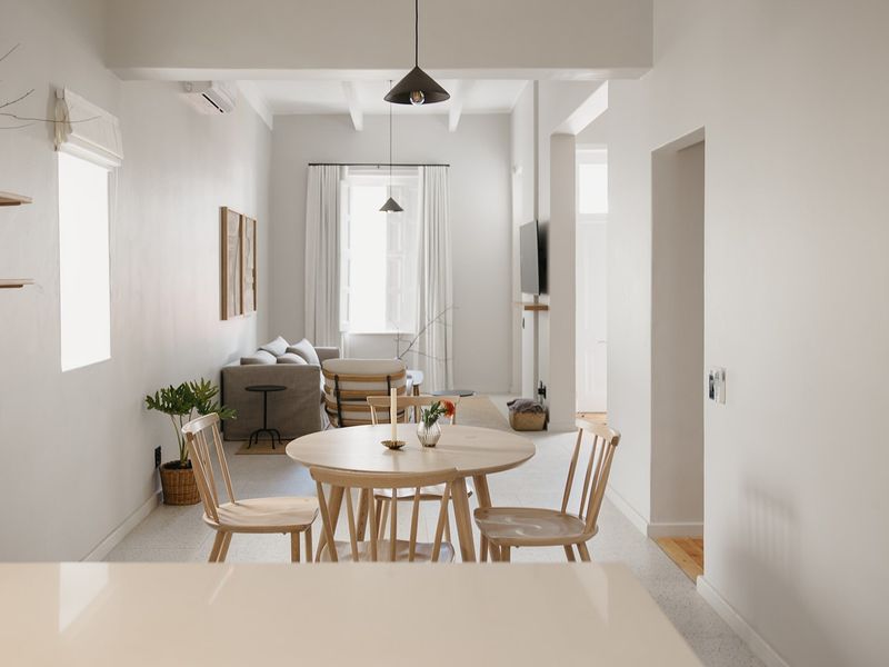 Bright open-plan living and dining area featuring high ceilings with exposed beams, terrazzo flooring, and modern pendant lighting.