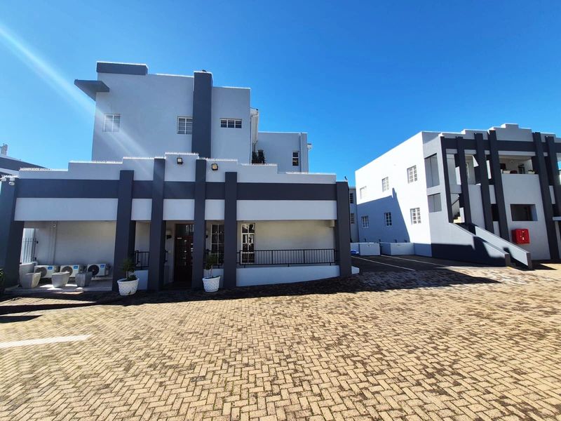 A well-maintained apartment complex exterior featuring modern grey and white facade detailing with a paved driveway and secure entrance area.