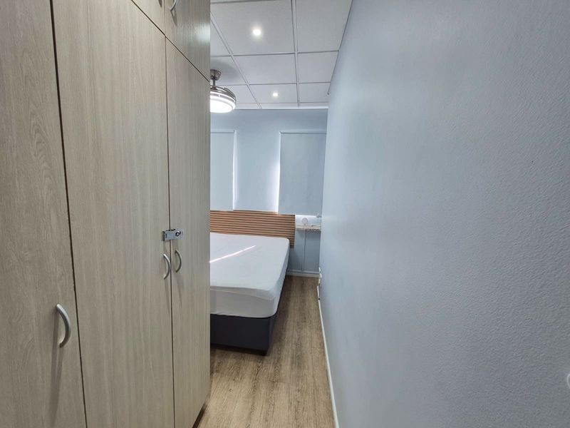 A bedroom featuring laminate flooring, built-in wardrobes, a drop ceiling with recessed lighting, and a ceiling fan.