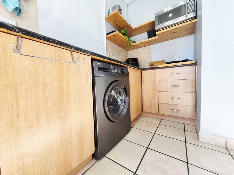 A functional laundry area featuring light wood cabinetry, dark laminate countertops, tiled flooring, and built-in shelving for storage.