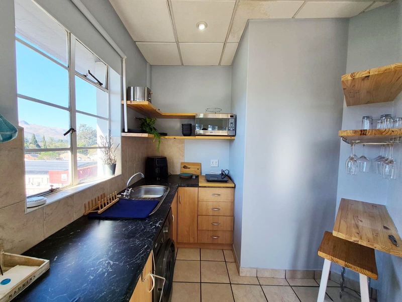 Compact kitchen featuring laminate countertops, stainless steel sink, built-in cabinetry, and floating timber shelving with a view of the surrounding area.