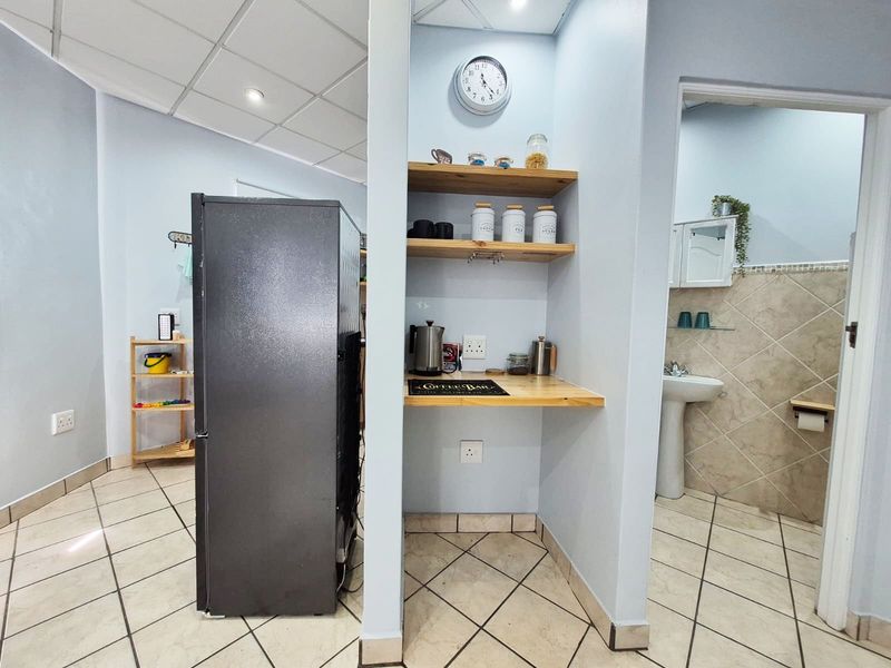 A functional kitchen area featuring tiled flooring, built-in wooden shelving, and an adjacent bathroom with a pedestal basin.