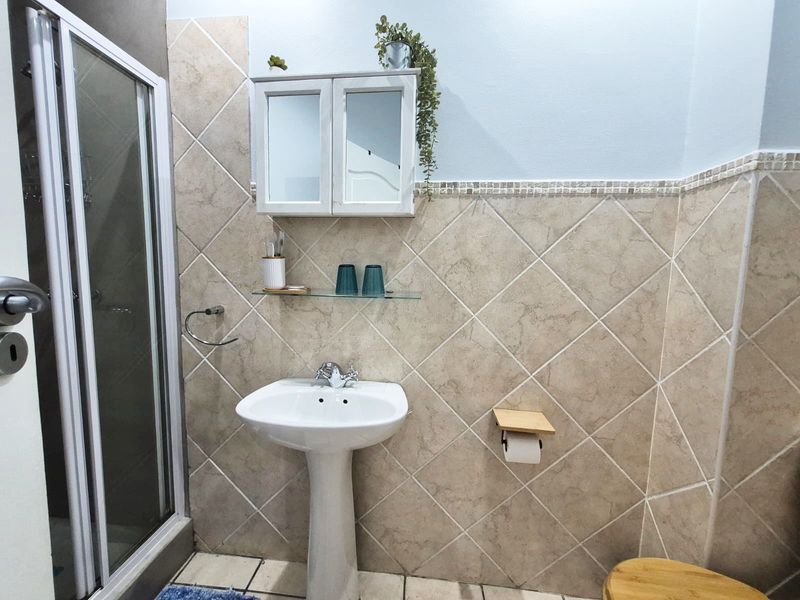 A functional bathroom featuring a pedestal basin, shower enclosure with glass doors, and tiled wall finishes with a built-in medicine cabinet.