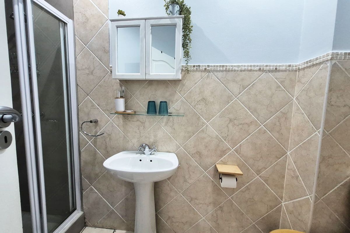 A functional bathroom featuring a pedestal basin, shower enclosure with glass doors, and tiled wall finishes with a built-in medicine cabinet.