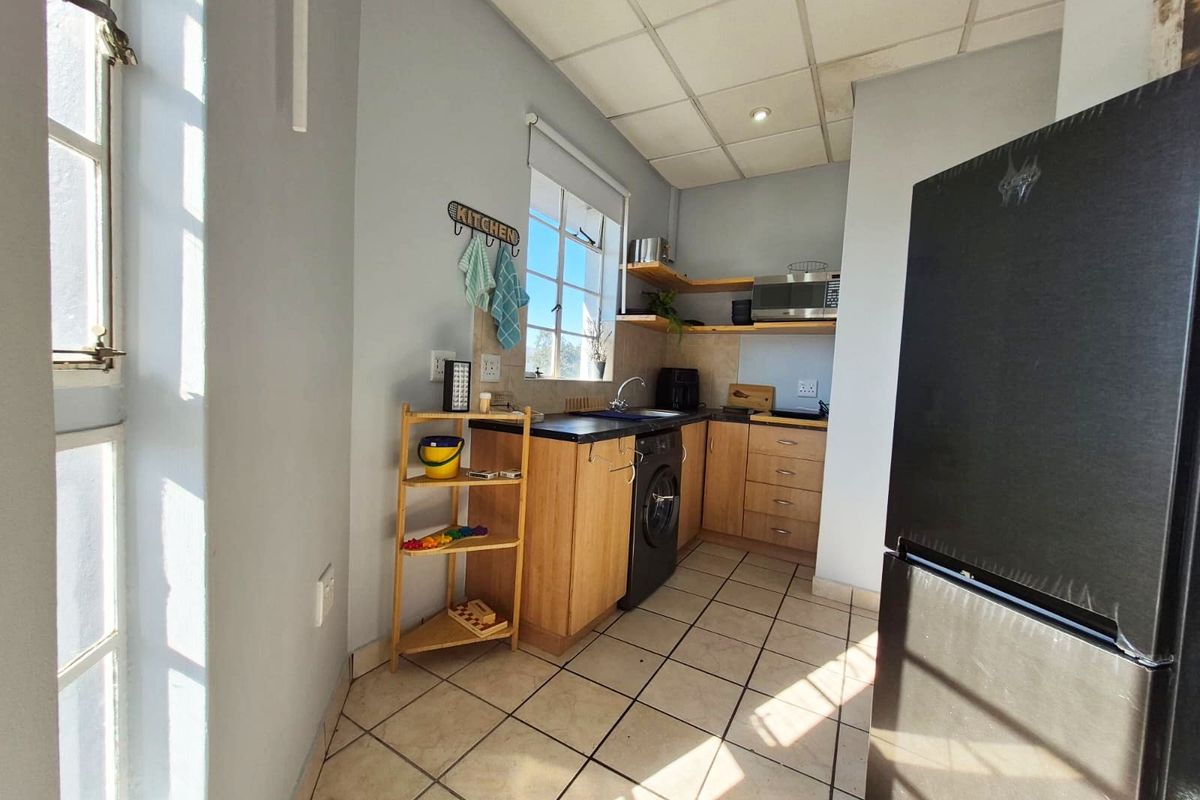 Compact kitchen featuring laminate cabinetry, dark countertops, integrated sink, and tiled flooring with a functional layout.