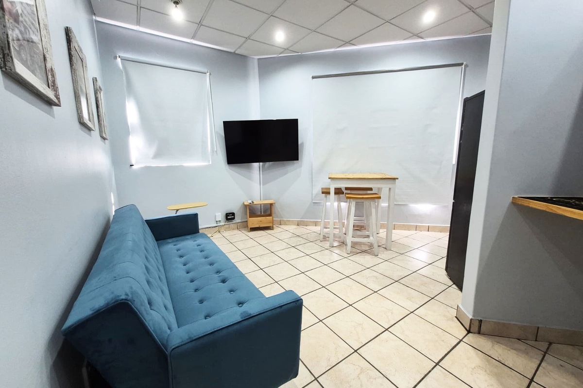 A living area featuring tiled flooring, a suspended ceiling with recessed lighting, and wall-mounted air conditioning.