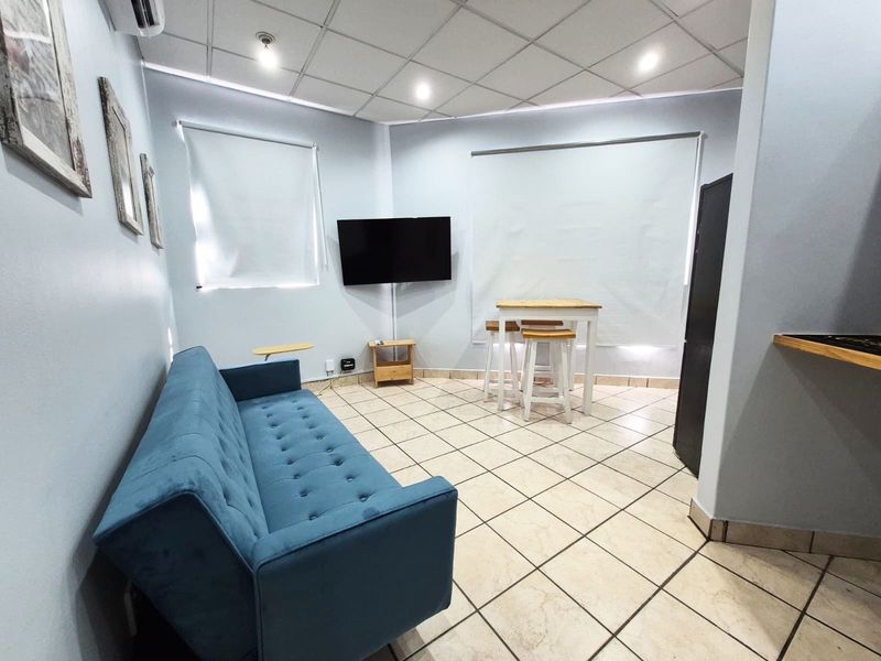 A living area featuring tiled flooring, a suspended ceiling with recessed lighting, and wall-mounted air conditioning.