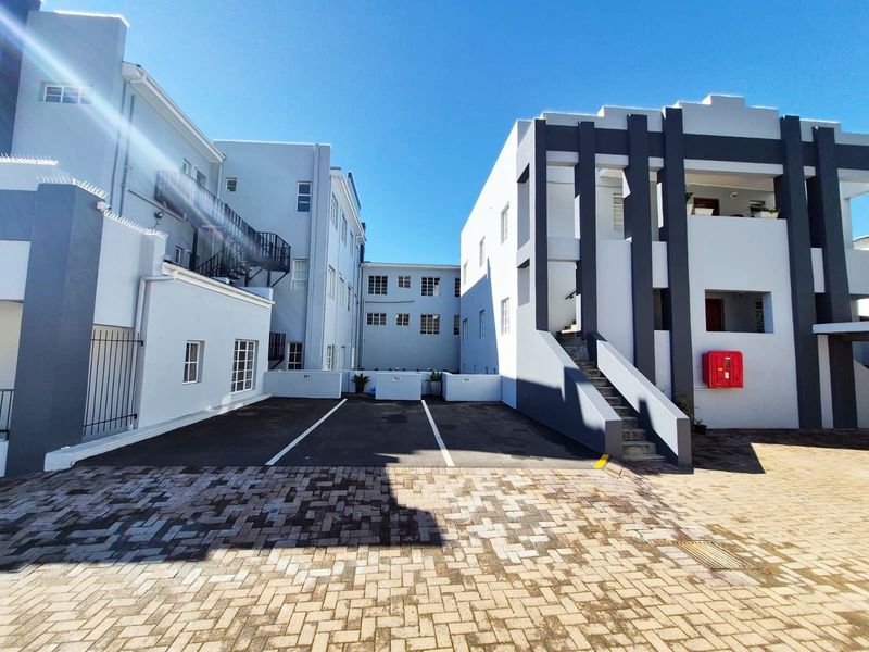Exterior view of the apartment complex featuring paved parking bays, external staircases, and modern building facade with security features.