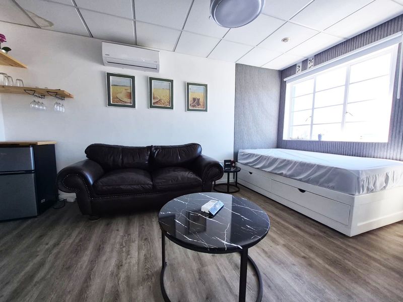 A bedroom featuring laminate flooring, a suspended ceiling with a water stain, and a wall-mounted air conditioning unit.