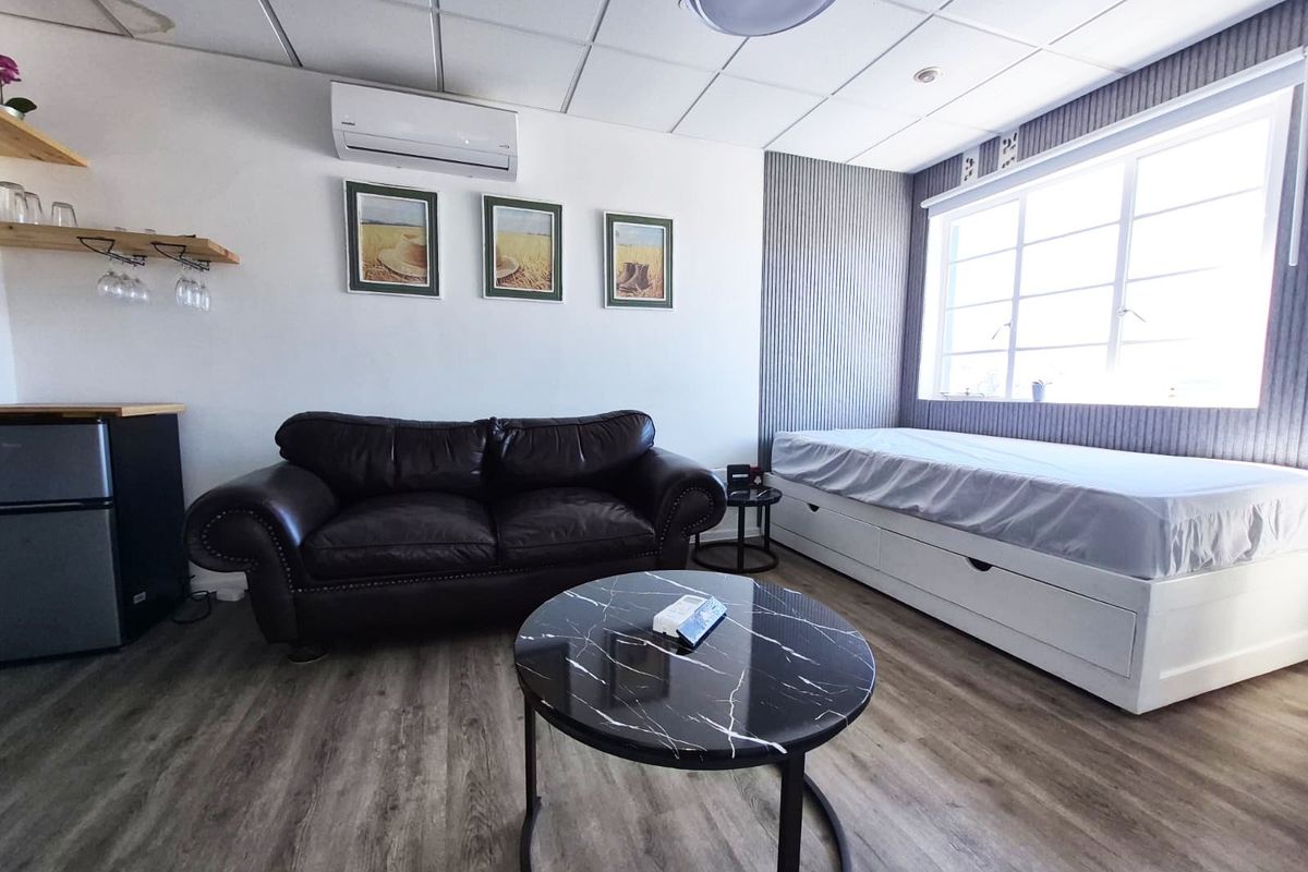 A bedroom featuring laminate flooring, a suspended ceiling with a water stain, and a wall-mounted air conditioning unit.