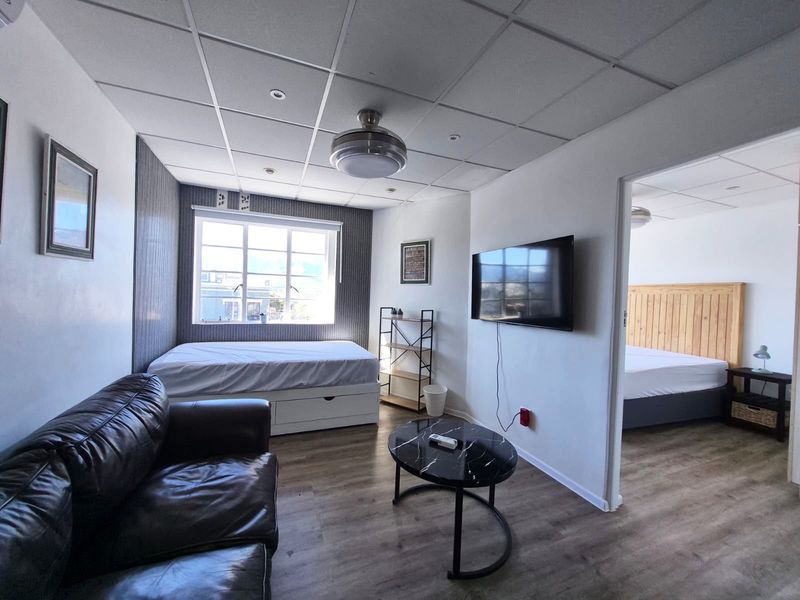 Open plan living area featuring laminate flooring, a suspended ceiling with integrated lighting, and a ceiling fan, with an adjoining bedroom visible.