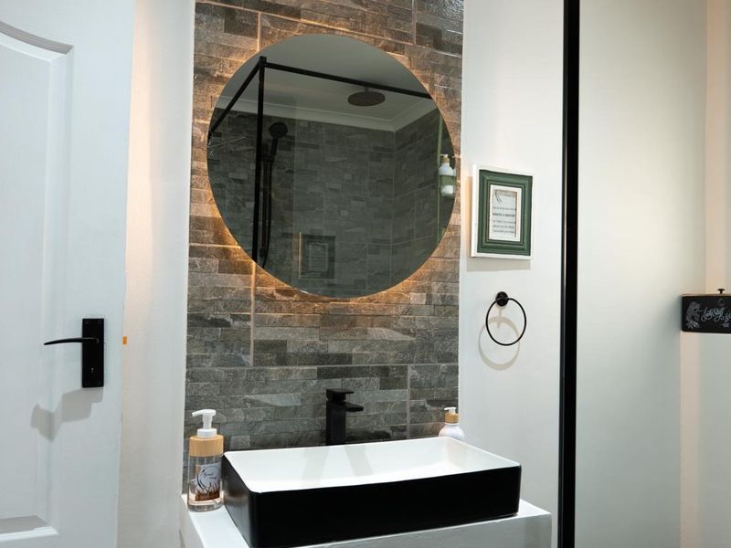 Modern bathroom featuring a stylish vessel sink, black fixtures, and a striking stone tile feature wall with a backlit circular mirror.