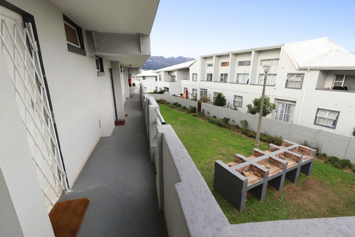 An elevated walkway overlooking a communal garden area featuring a built-in brick braai facility within an apartment complex.