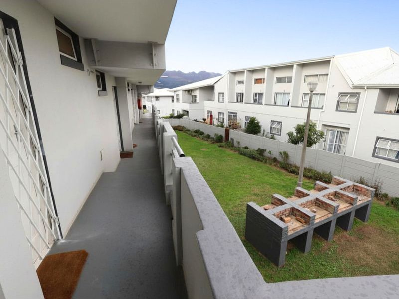 An elevated walkway overlooking a communal garden area featuring a built-in brick braai facility within an apartment complex.