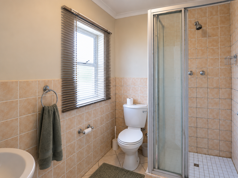 A functional bathroom featuring a shower enclosure, toilet, and neutral tiled finishes, offering a clean and practical space.