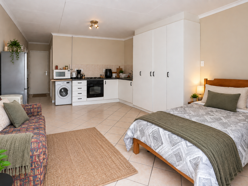A functional open-plan studio apartment featuring a compact kitchen with built-in appliances, tiled flooring, and integrated wardrobe storage.