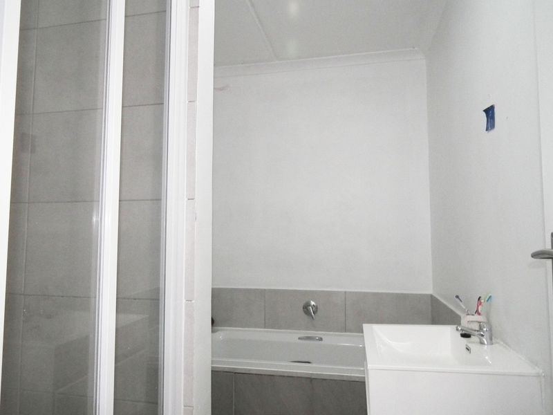 A functional bathroom featuring a built-in bathtub, a modern vanity basin, and a separate shower enclosure with neutral wall tiling.