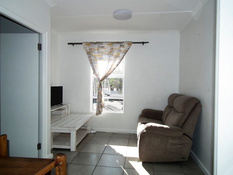 A compact living room featuring tiled flooring, a central window, and a ceiling light fixture.