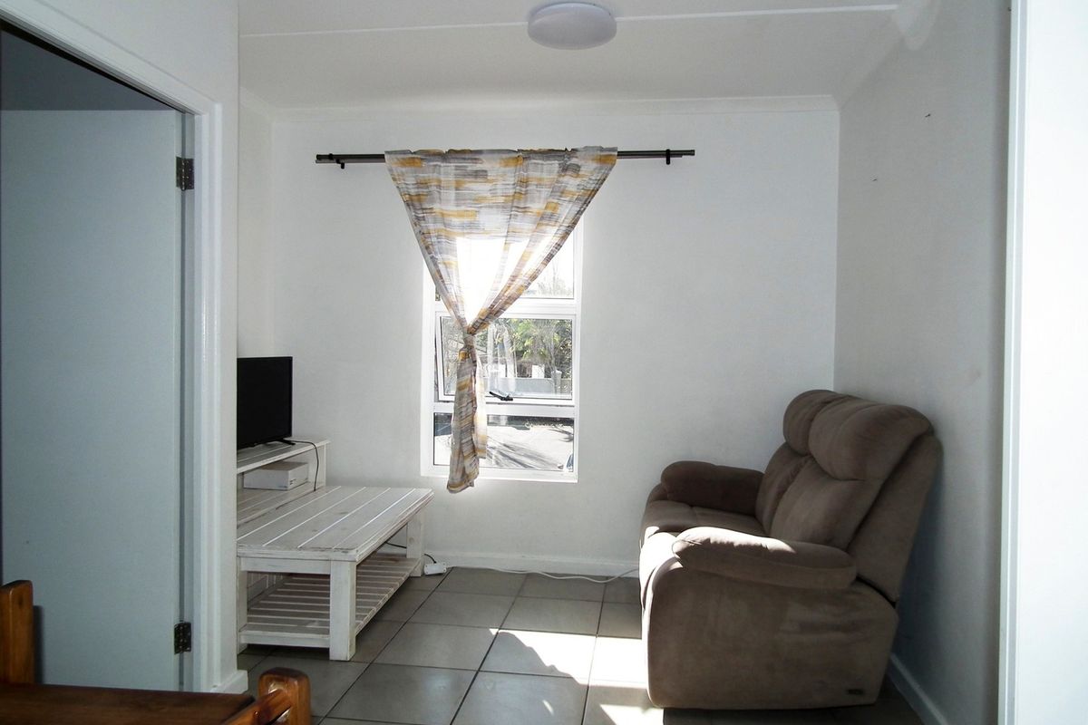 A compact living room featuring tiled flooring, a central window, and a ceiling light fixture.