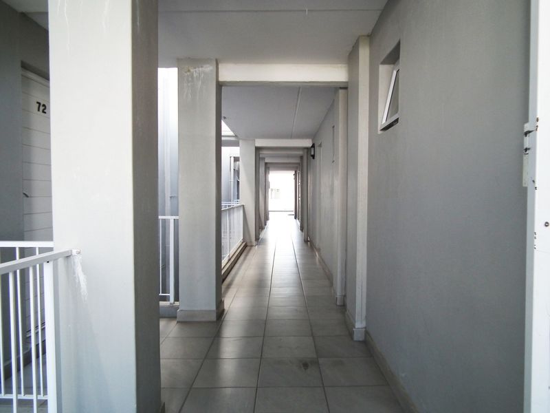 A functional apartment building hallway featuring tiled flooring, structural columns, and metal balustrades, providing access to residential units.