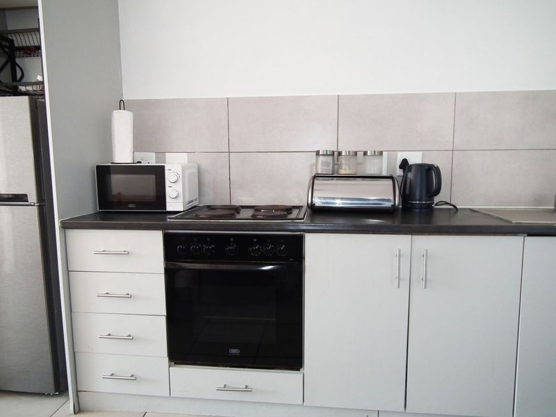 A functional kitchen featuring built-in cabinetry, a dark laminate countertop, a tiled backsplash, and a built-in oven with an electric hob.