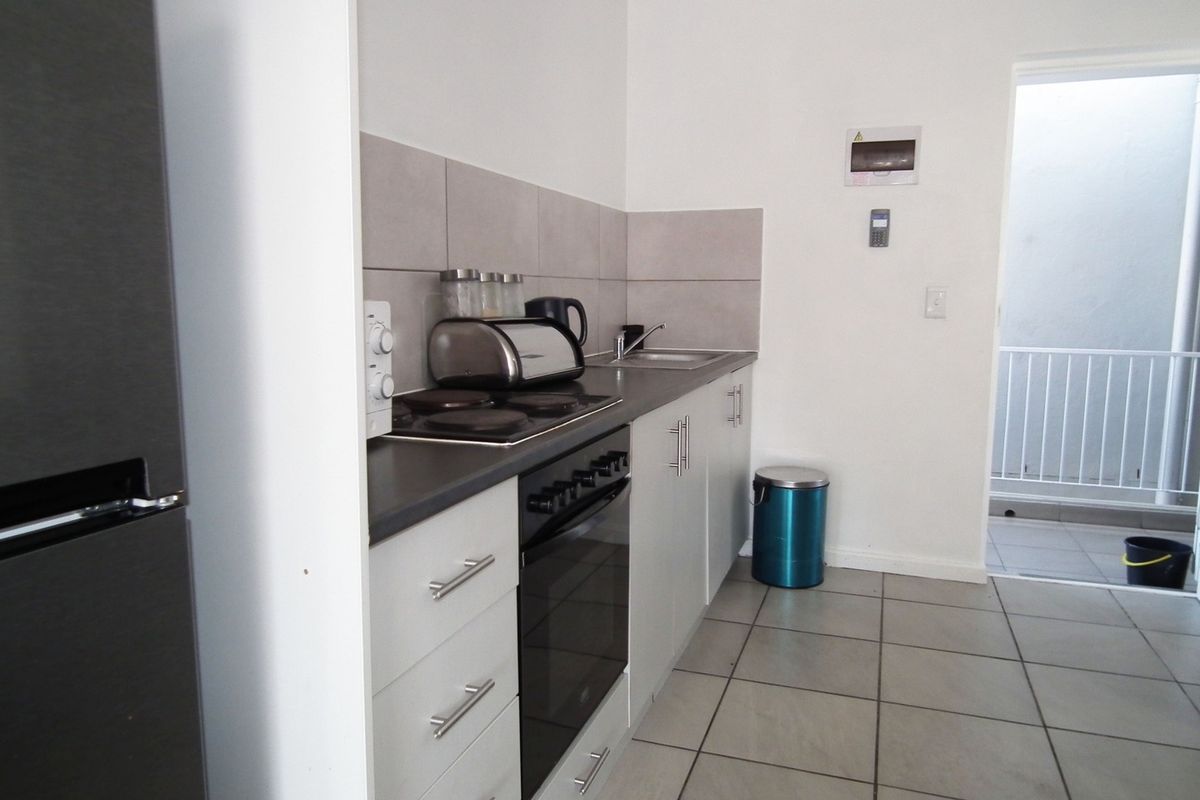 A compact, functional kitchen featuring modern cabinetry, a built-in oven and hob, tiled backsplash, and neutral floor tiles with direct access to an outdoor area.
