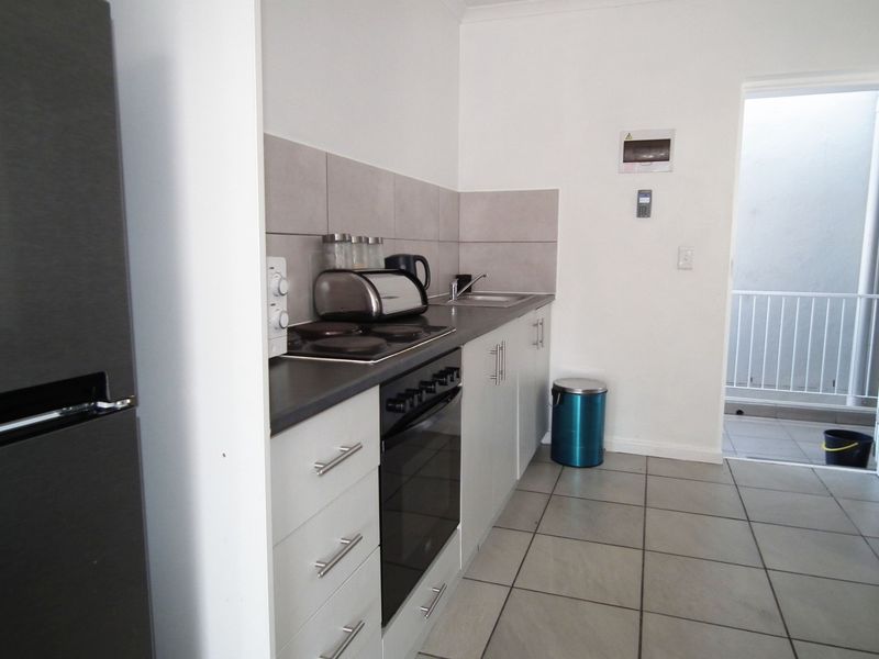 A compact, functional kitchen featuring modern cabinetry, a built-in oven and hob, tiled backsplash, and neutral floor tiles with direct access to an outdoor area.