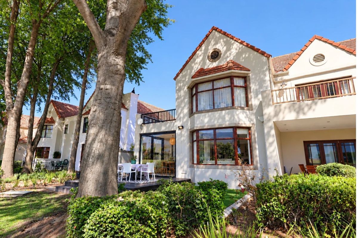 Rear view of a multi-story residential property featuring terracotta roof tiles, bay windows, a balcony, and a paved patio area set within a garden.