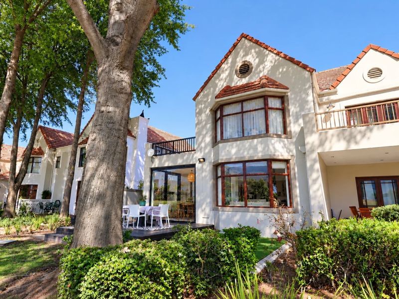 Rear view of a multi-story residential property featuring terracotta roof tiles, bay windows, a balcony, and a paved patio area set within a garden.