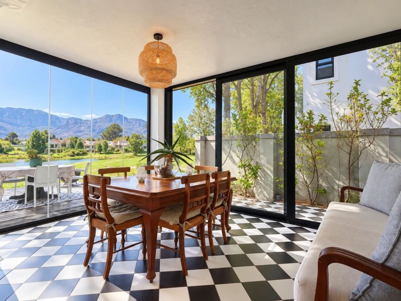 A bright, enclosed patio featuring floor-to-ceiling glass walls, checkered tile flooring, and scenic views of the surrounding landscape.