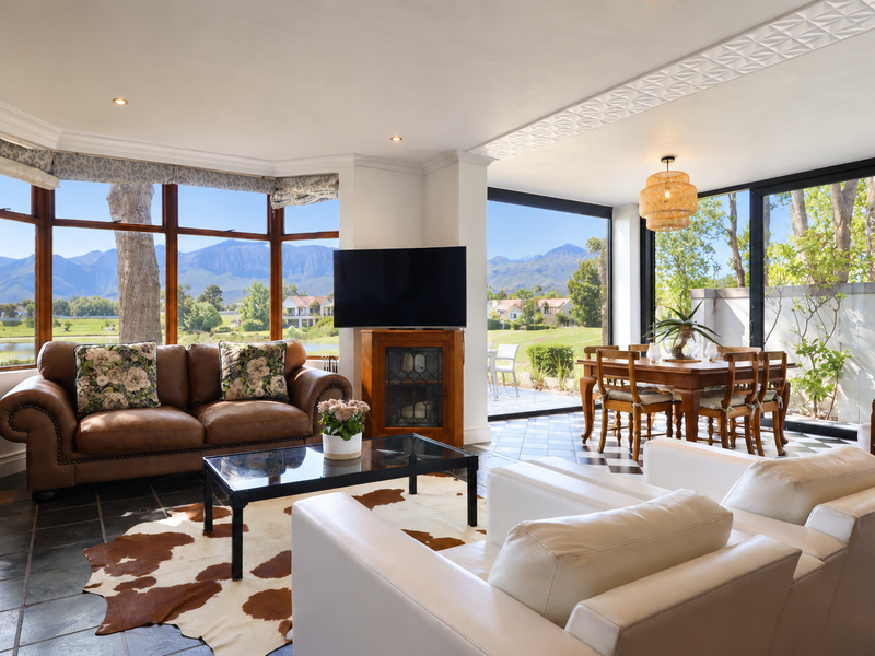 Spacious open-plan living and dining area featuring large windows and sliding doors with scenic mountain and golf course views, complemented by stone tile flooring.