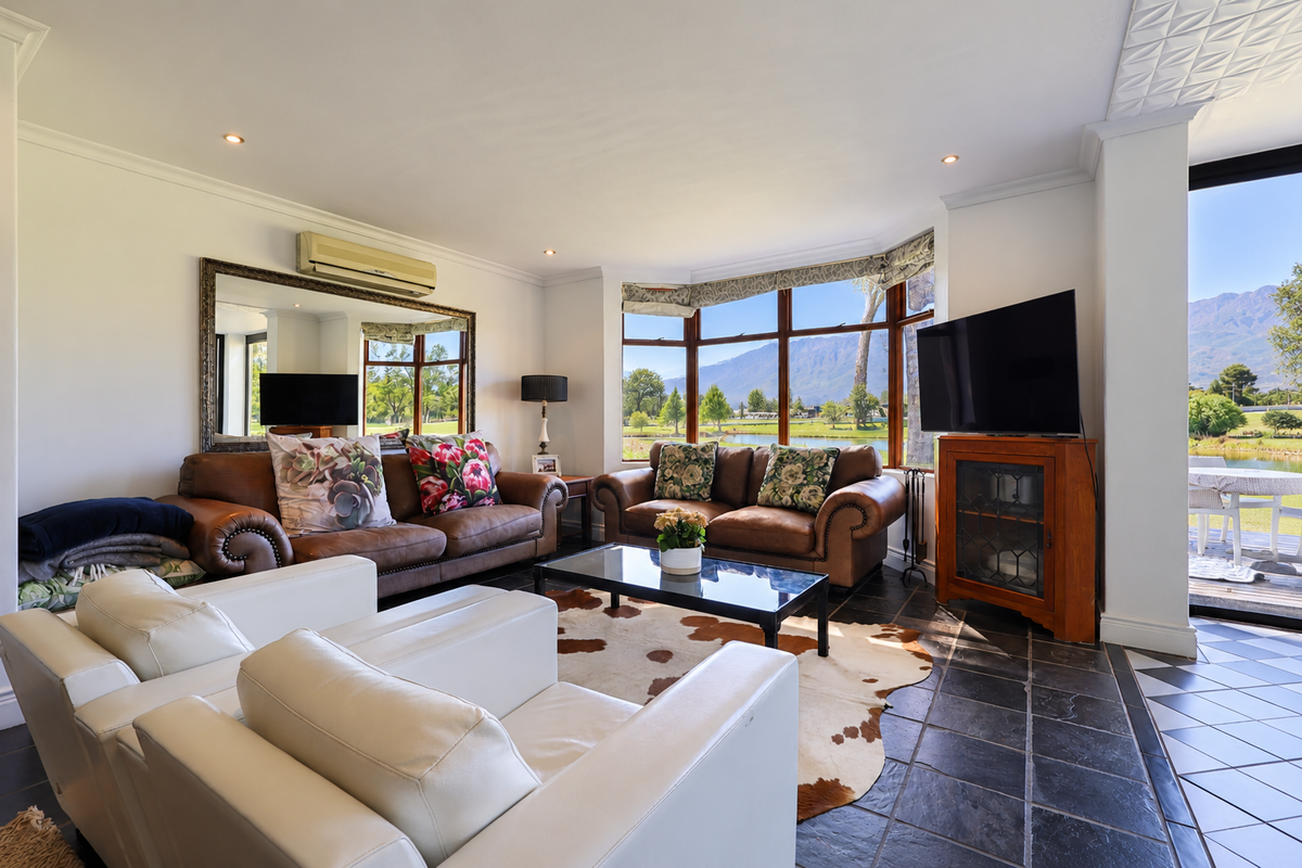 Spacious living room featuring large bay windows with scenic views, tiled flooring, and direct access to an outdoor patio area.