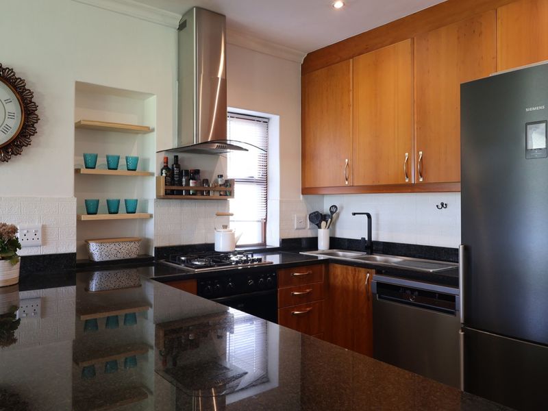A well-maintained kitchen featuring wooden cabinetry, granite countertops, a gas hob with extractor fan, and integrated appliances.