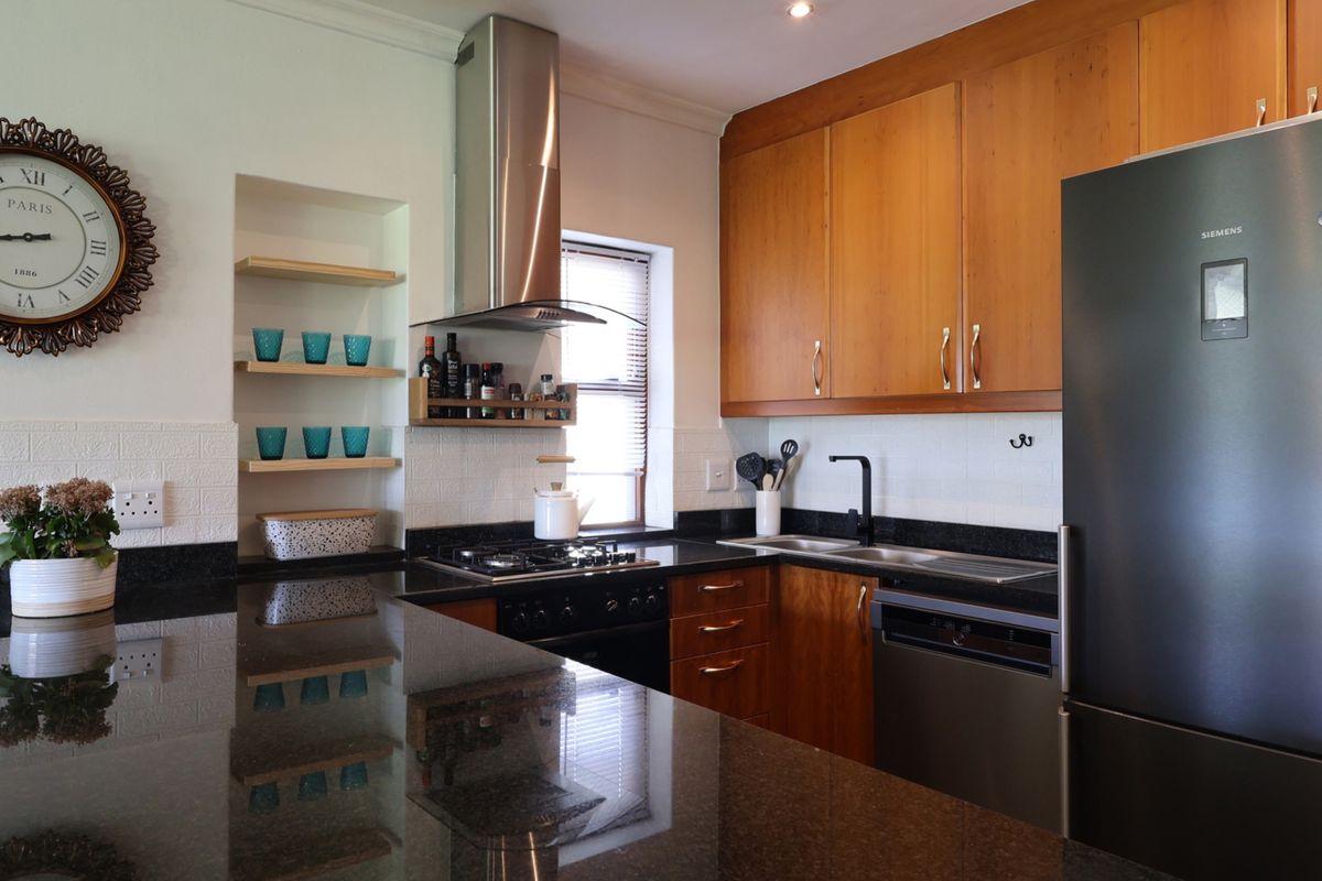 A well-maintained kitchen featuring wooden cabinetry, granite countertops, a gas hob with extractor fan, and integrated appliances.