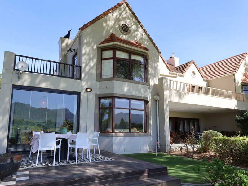 Rear elevation of a multi-story residence featuring a timber deck, balcony, bay windows, and a well-maintained garden area with artificial lawn.