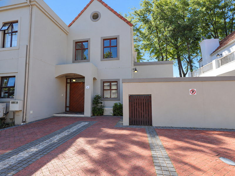 Front elevation of a two-story residence featuring a paved driveway, timber entrance door, and a secure boundary wall with a side gate.